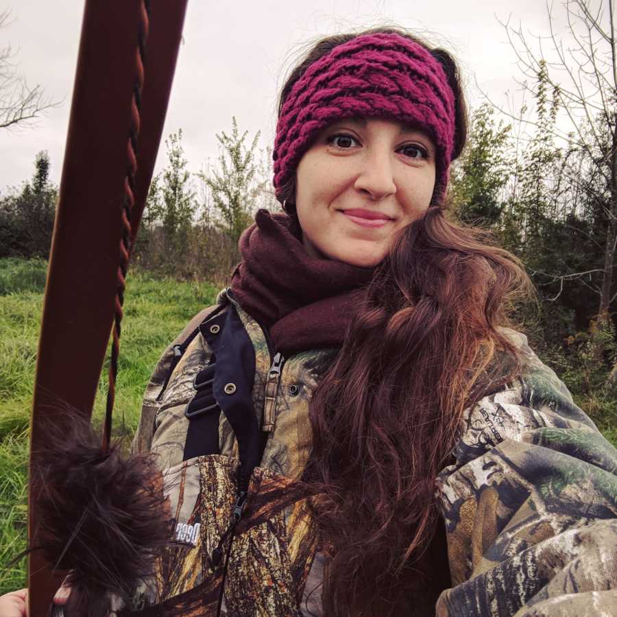 Pregnant woman smiles in selfie in camo jacket holding bow and arrow