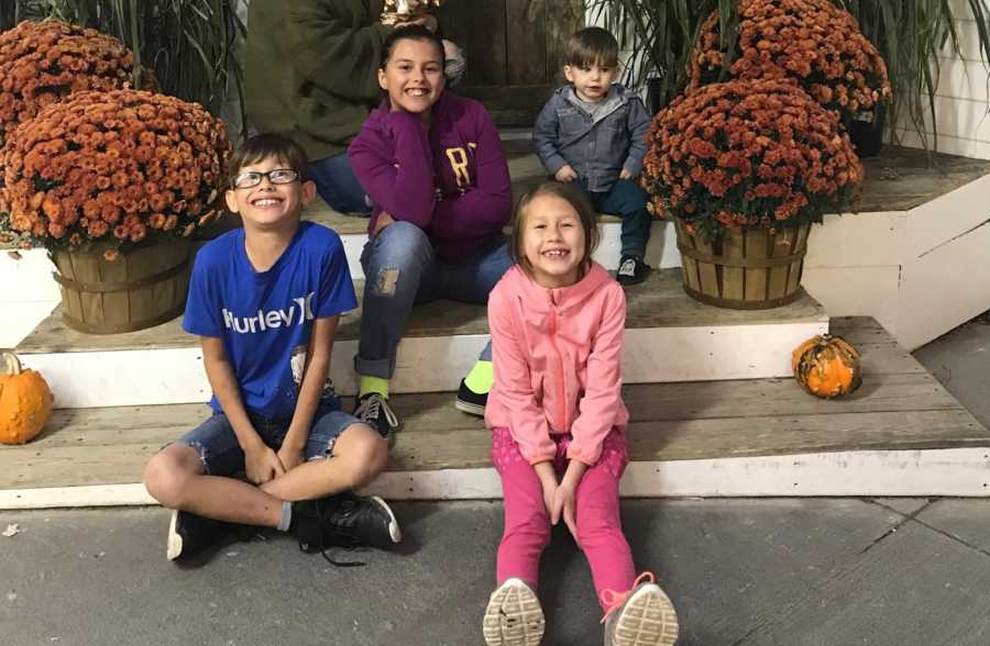 Four children that were in foster care and are now adopted sit on outdoor steps of home beside pumpkin and flowers