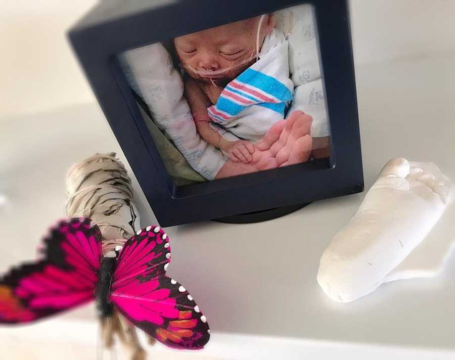 Clay mold of baby with HLH foot beside picture frame of baby and fake butterfly