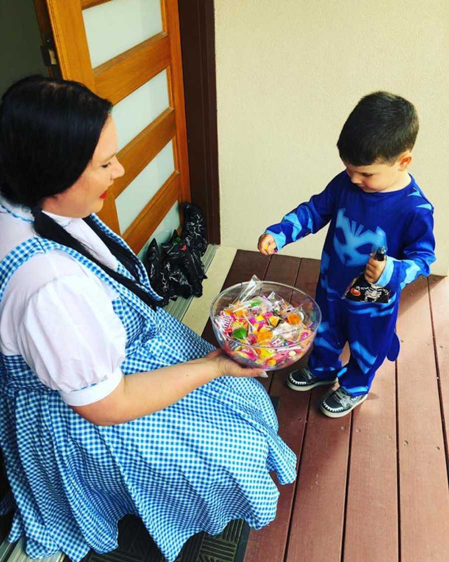 Woman dressed as Dorothy from Wizard of Oz kneels with bowl of candy for trick-or-treater