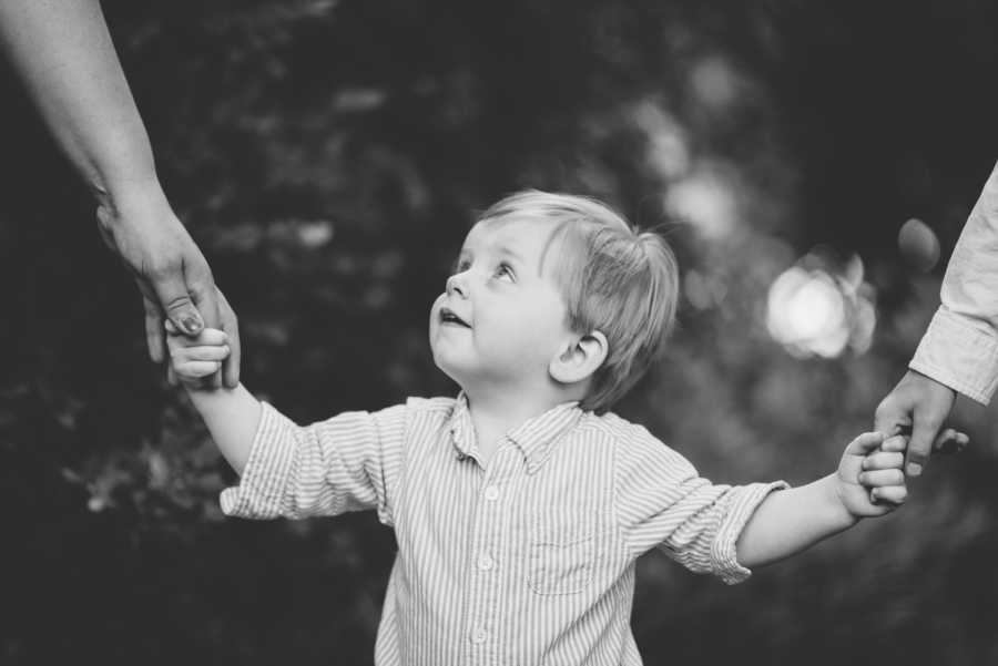 Toddler holding hands of parents and looking up at mother