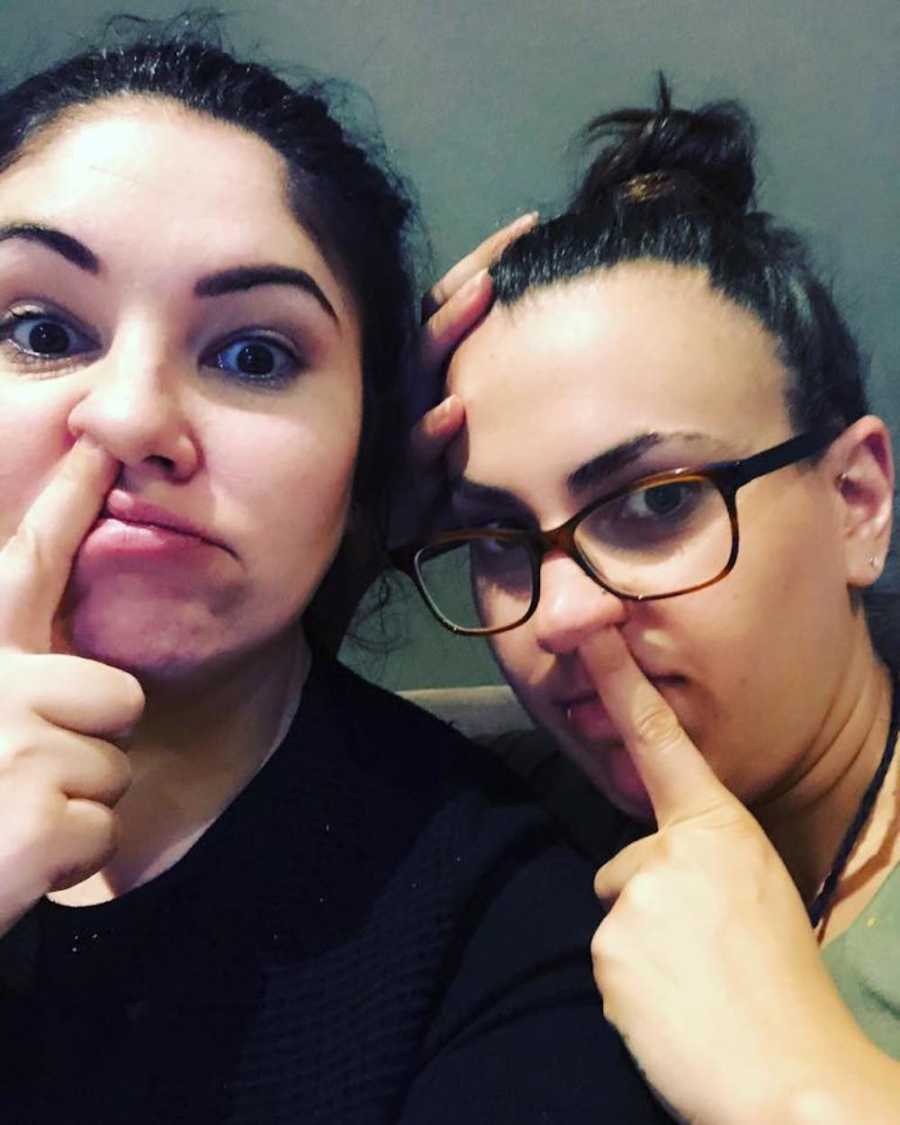 Two women sit side by side with finger up their nose in selfie