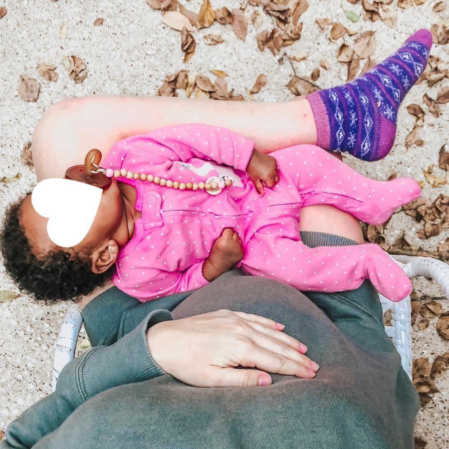 Pregnant mother sits on ground beside leaves while foster baby sleeps on her lap