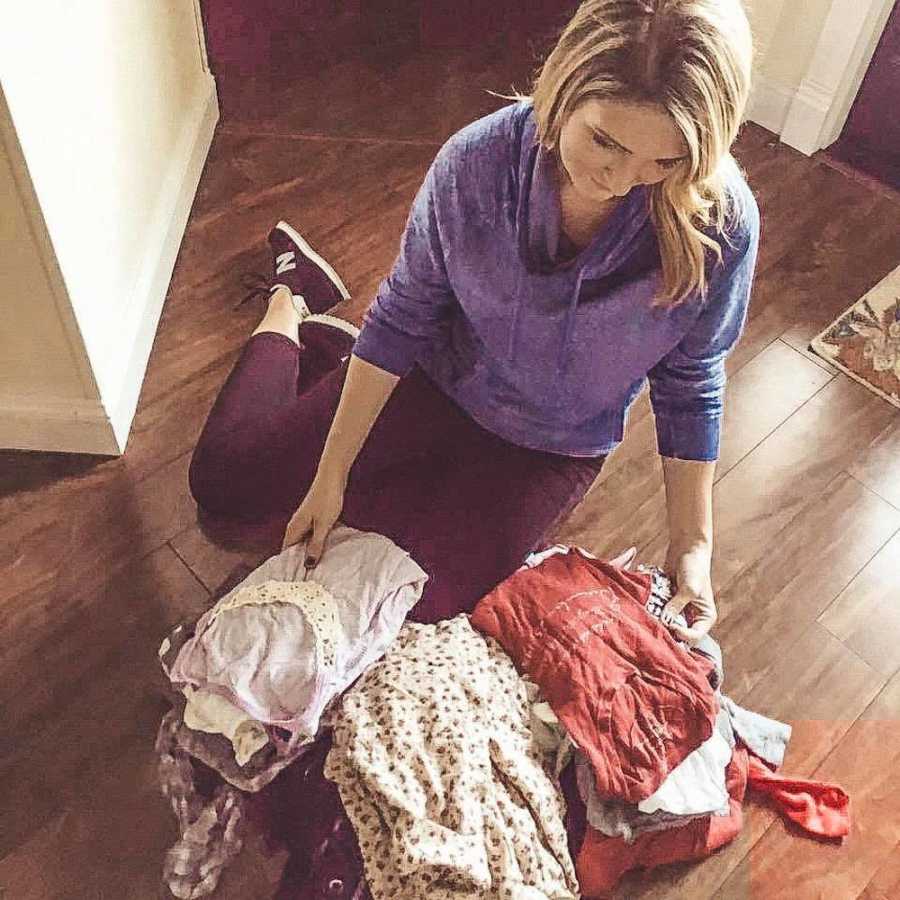 Mother sits on floor of home with three piles of folded laundry in front of her
