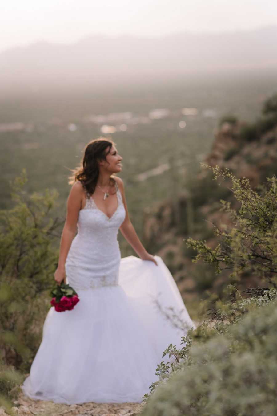 Woman in wedding gown stands on mountain holding bouquet of red roses