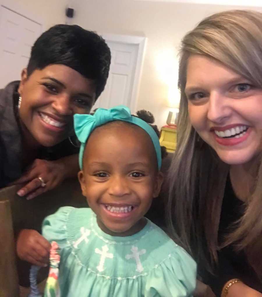 Woman smiles in selfie with adopted African American daughter and African American woman who teaches mother to do her hair