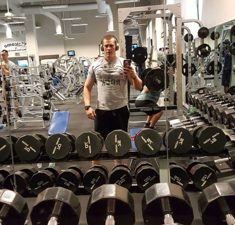 Active duty service member takes mirror selfie in gym behind weights