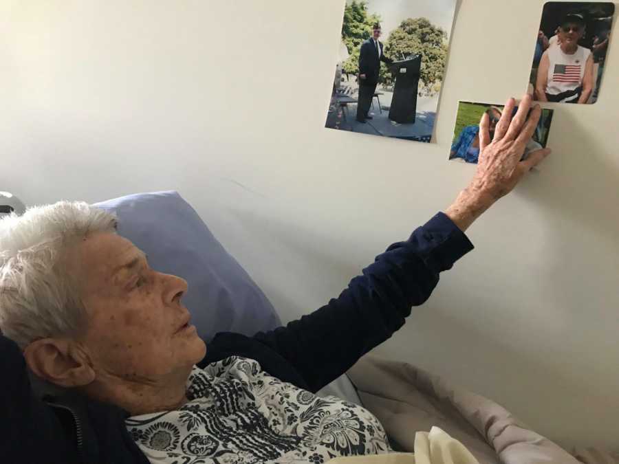 Elderly woman with dementia lays in bed in nursing home touch pictures on wall beside her