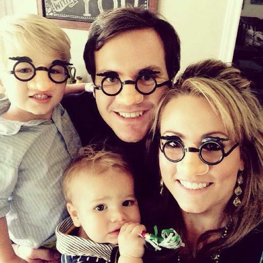 Husband and wife smile in selfie with their two sons while they were costume glasses with big nose