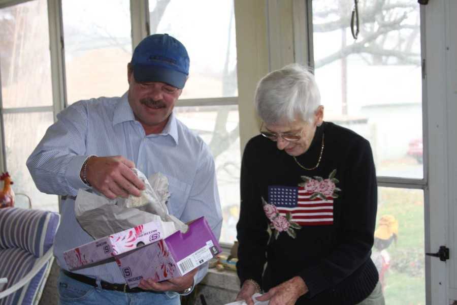 Man opens up shoe box in home beside elderly mother with dementia