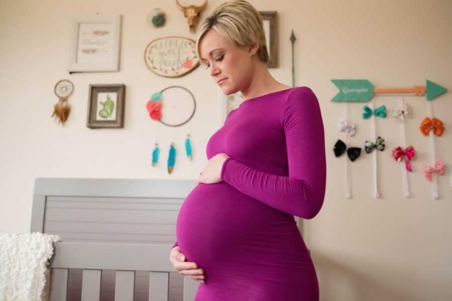 Pregnant woman who had an egg donor holds her stomach next to crib in baby's nursery