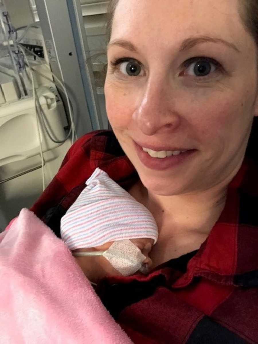 Woman smiles in selfie while holding preemie baby tight to her chest