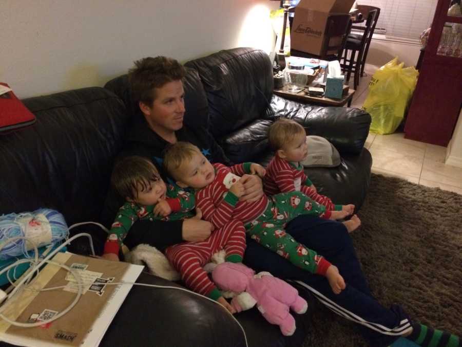 Man sits on couch with triplets in matching Christmas pj's on his lap