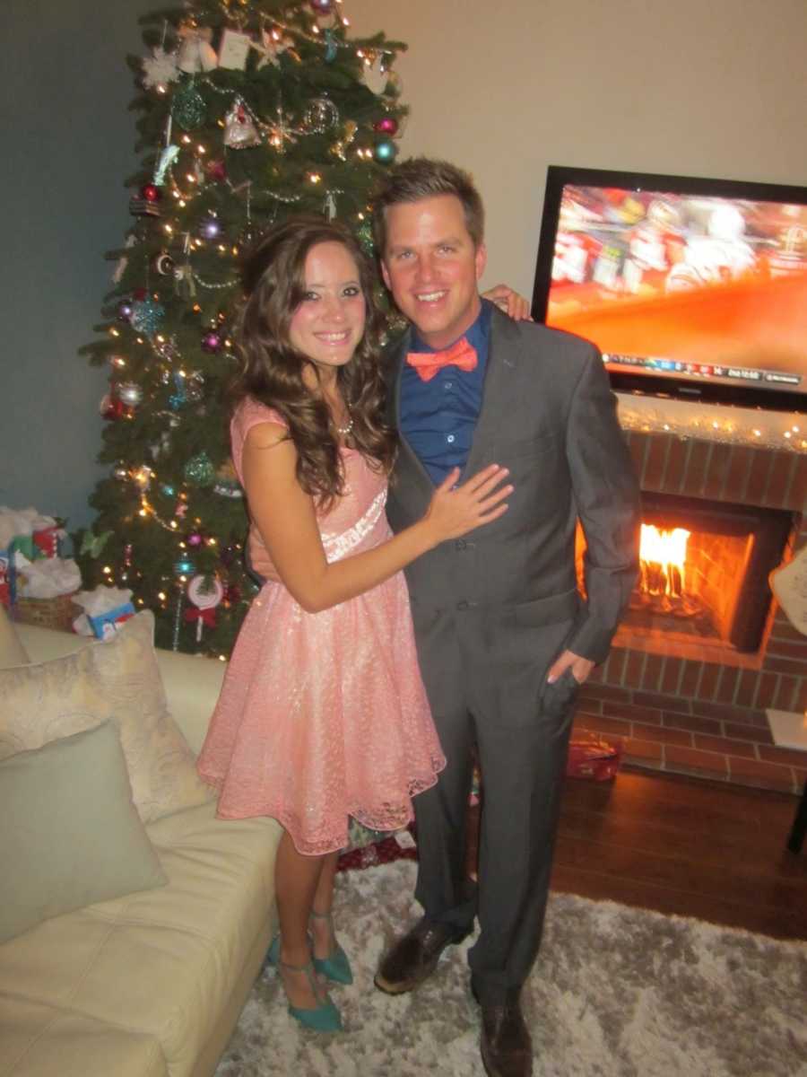 Married couple stands arm in arm in home standing in front of Christmas tree