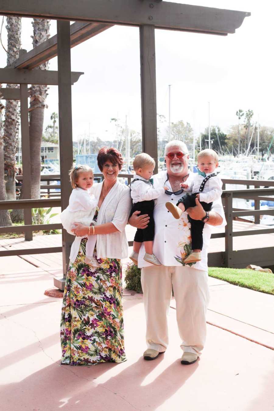 Husband and wife stand outside holding triplets in their arms