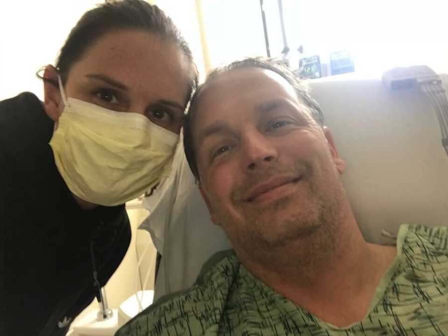 Wife with yellow mask on smiles in selfie with husband in hospital who went into cardiac arrest