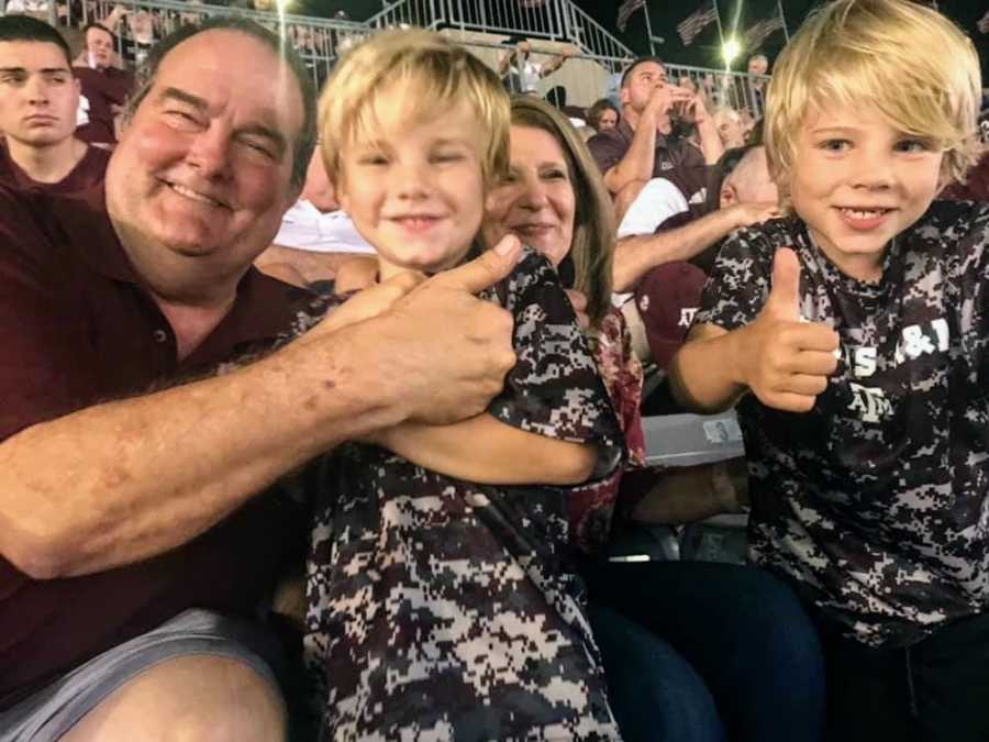 Man who has since passed with with grandsons in football stadium with thumbs up