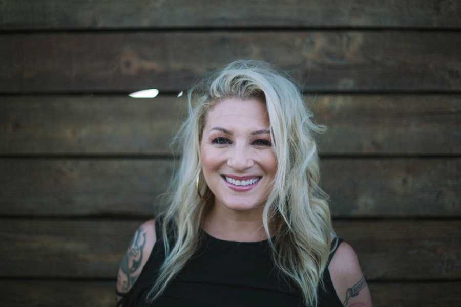 Woman who got sober smiles outside in front of wood wall