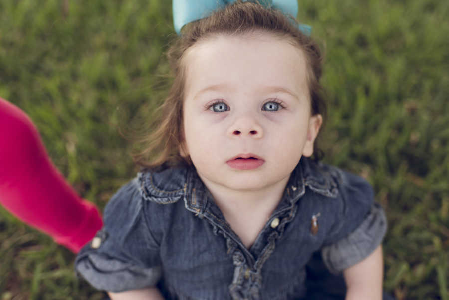 Adopted little girl in denim top and big blue bow in her hair looks up