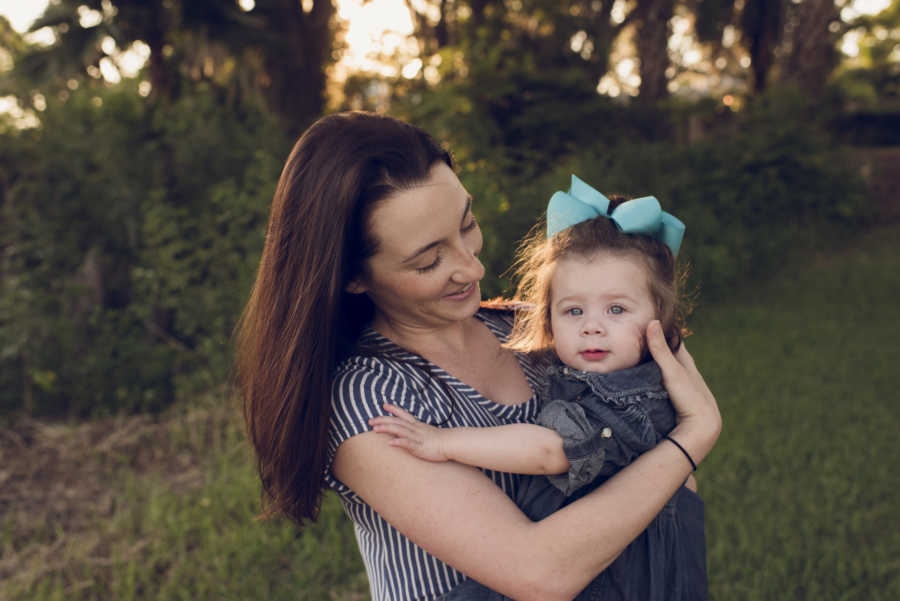 Mother stands outside smiling while holding her adopted daughter