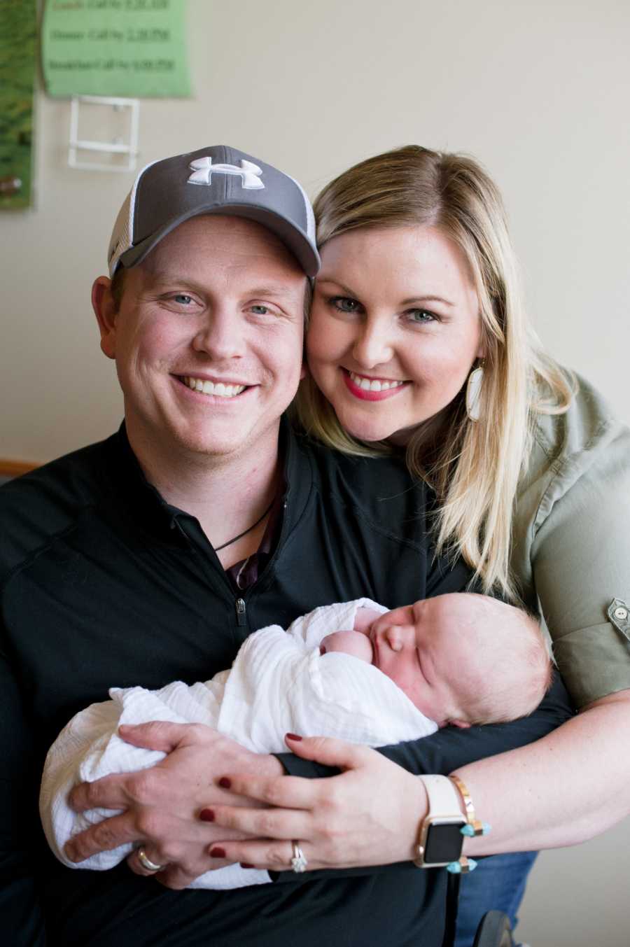 Husband in wheelchair holds adopted newborn while wife stands beside him 