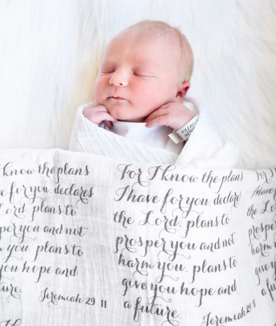 Newborn adopted baby laying on back swaddled in blanket with message written on it