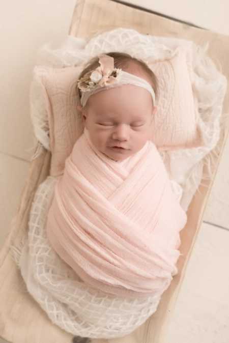 Baby girl who was carried by surrogate swaddled in pink blanket lying on blankets and pillow