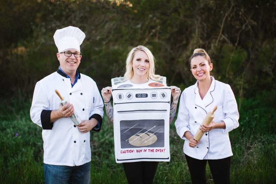 Parents of child stand in chefs coats and hats while surrogate stands between them in oven costume