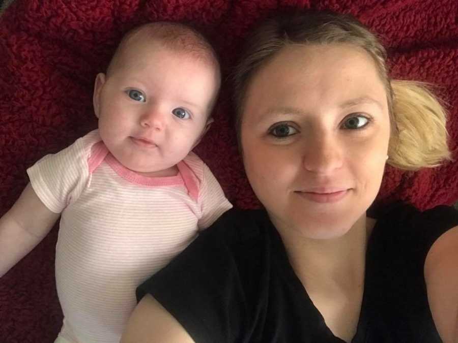 Mother lays on her back smiling in selfie with her daughter who has shaken baby syndrome