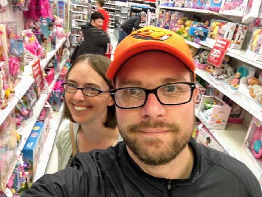 Husband and wife smile in selfie in toy aisle shopping for children's Christmas presents
