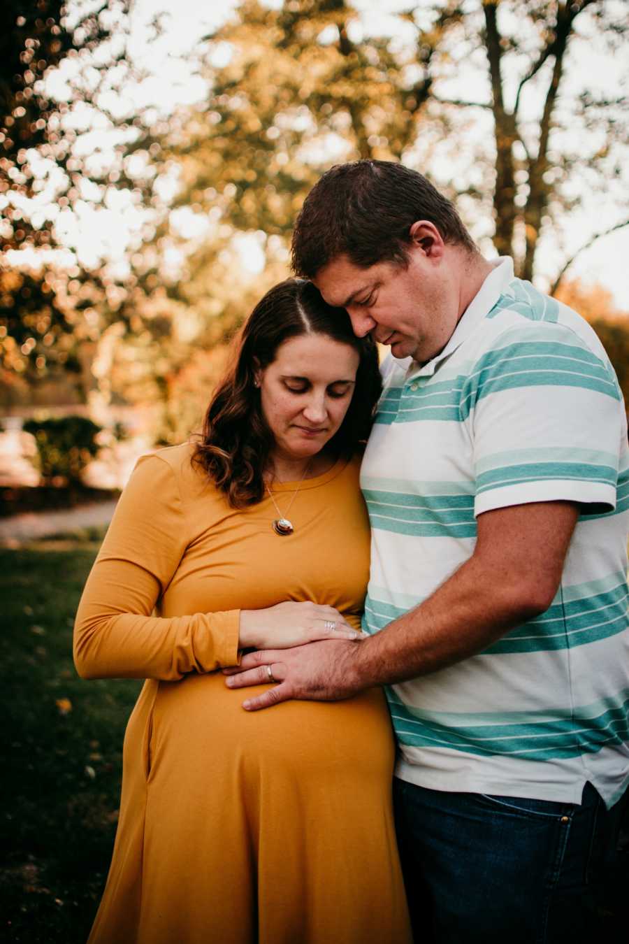 Pregnant birth photographer stands outside with husband as they both touch her stomach
