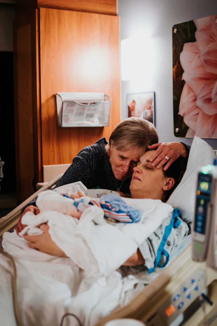 Woman lays in hospital bed holding her newborn that will soon die with her mother standing beside her