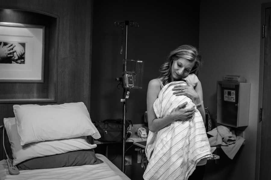 Woman stands holding adopted newborn in hospital room