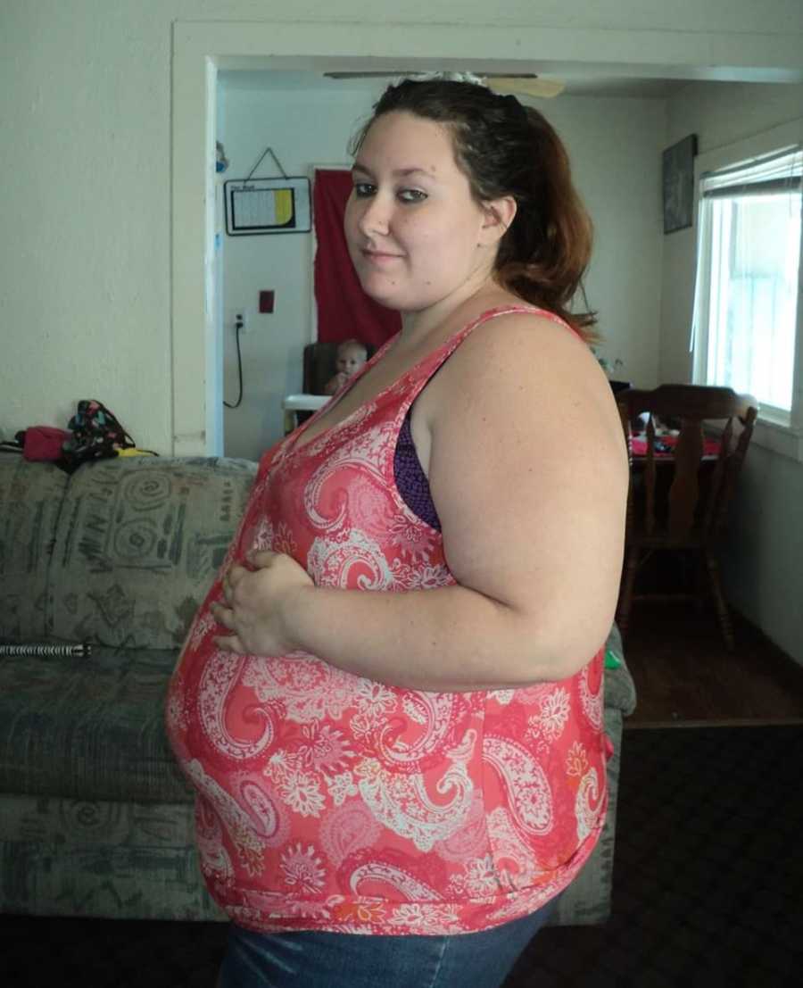 Pregnant woman stands holding her stomach in home