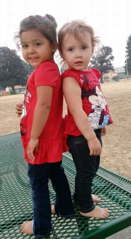 Toddlers whose mothers are cousins stand back to back on picnic table in matching outfits