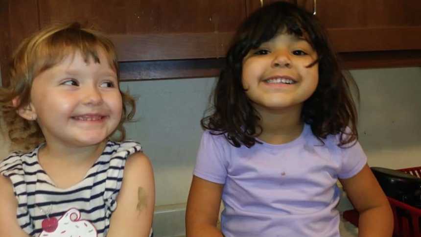 Toddlers whose mothers are cousins sit smiling beside each other