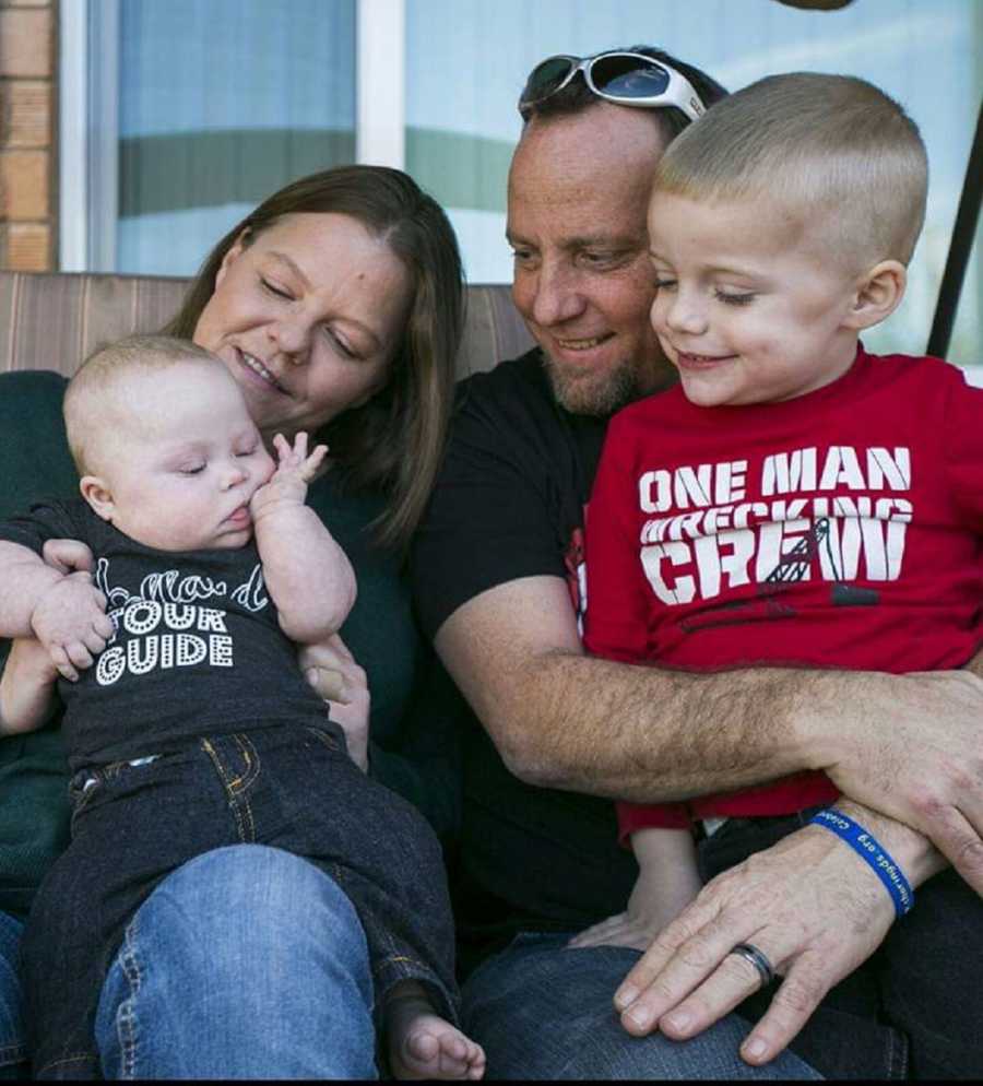 Husband and wife sit outside with their older son and younger son with down syndrome who defeated cancer