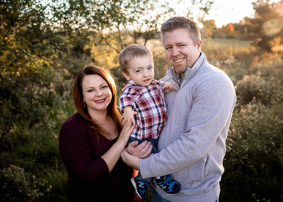 Husband and wife stand outside holding son with dwarfism