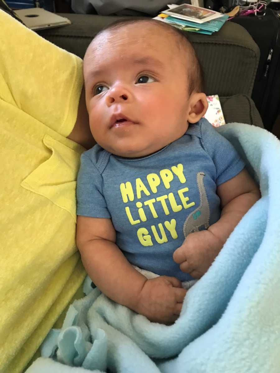 Baby with shaken baby syndrome lays in someone's lay wearing shirt that says, "happy little guy"