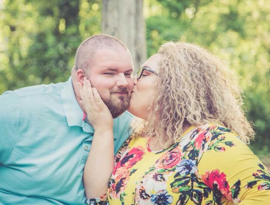 Wife stands outside holding husbands face as she kisses him on cheek