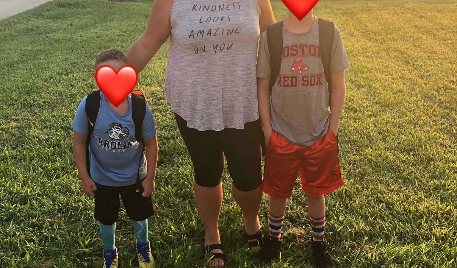 Woman stands outside with arms around two foster sons who both have red heart emojis covering their face