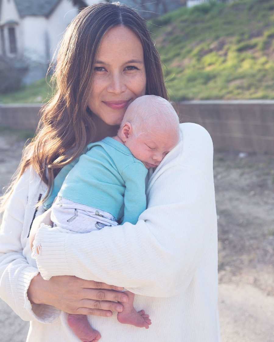 Mother stands smiling while holding albino baby in her arms