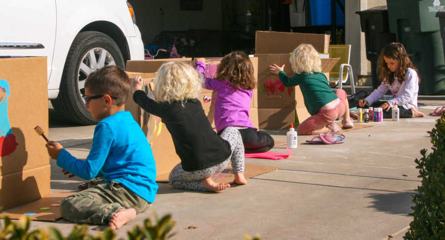 Five young children sitting in driveway painting on boxes they will wear for their own Thanksgiving Day parade