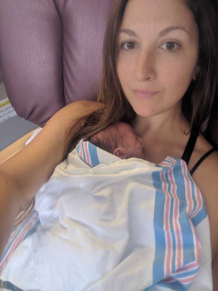 Mother smiles in selfie in NICU with newborn asleep on her chest