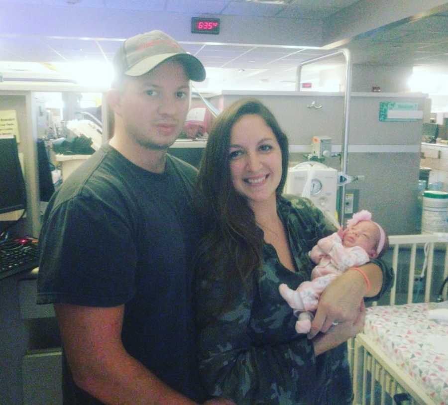 Mother stands in NICU holding baby girl beside husband who they can finally take home