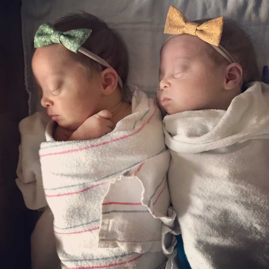 Newborn twins sleeping while swaddled in blankets with green and yellow bow headbands