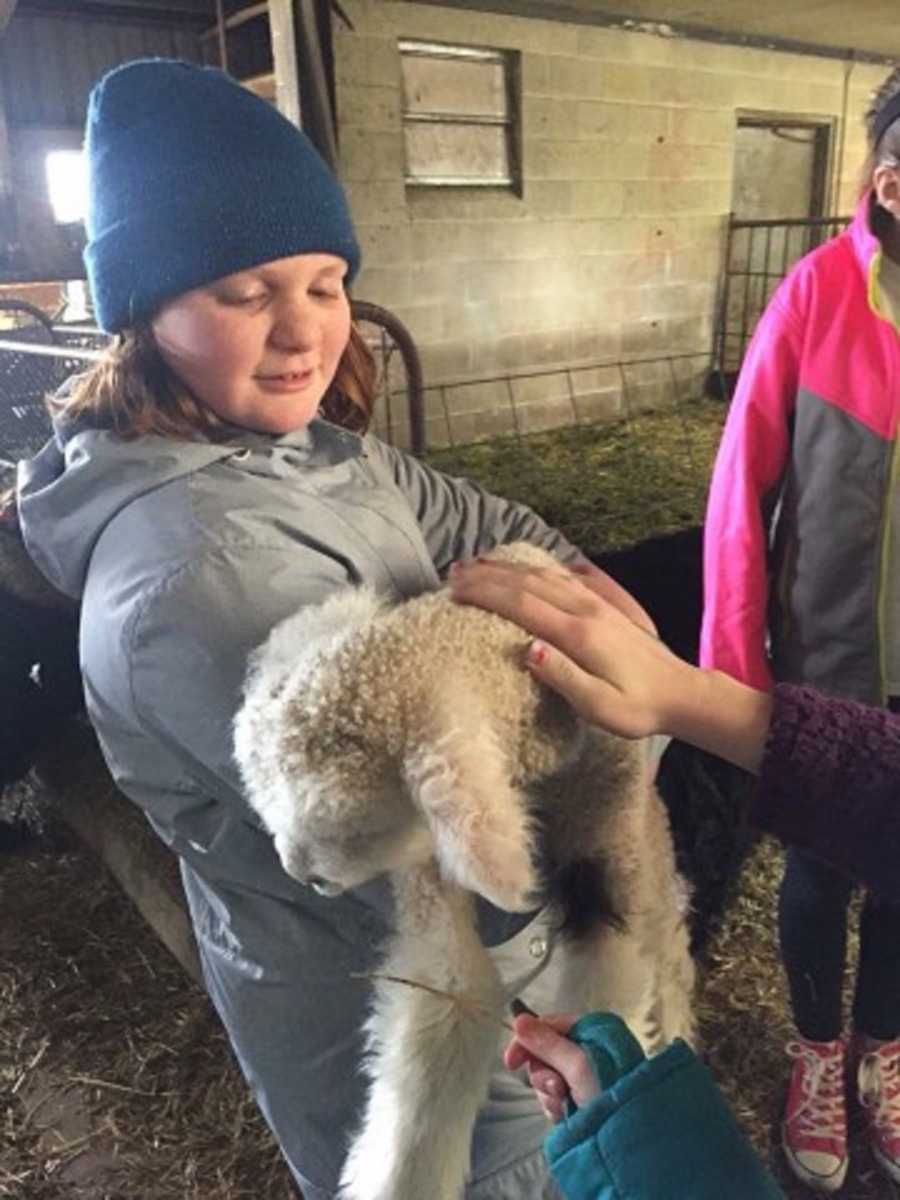Young girl who is tall for her age stands in barn holding baby sheep