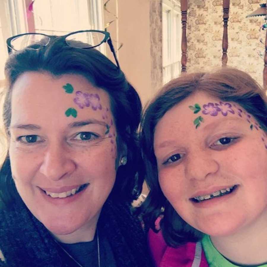 Mother smiles in daughter in selfie with purple flowers painted on their face