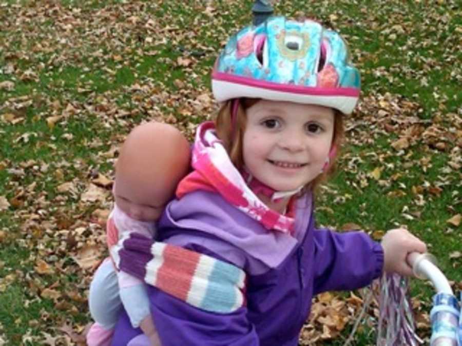 Young girl wearing helmet on bicycle with baby doll wrapped to her back
