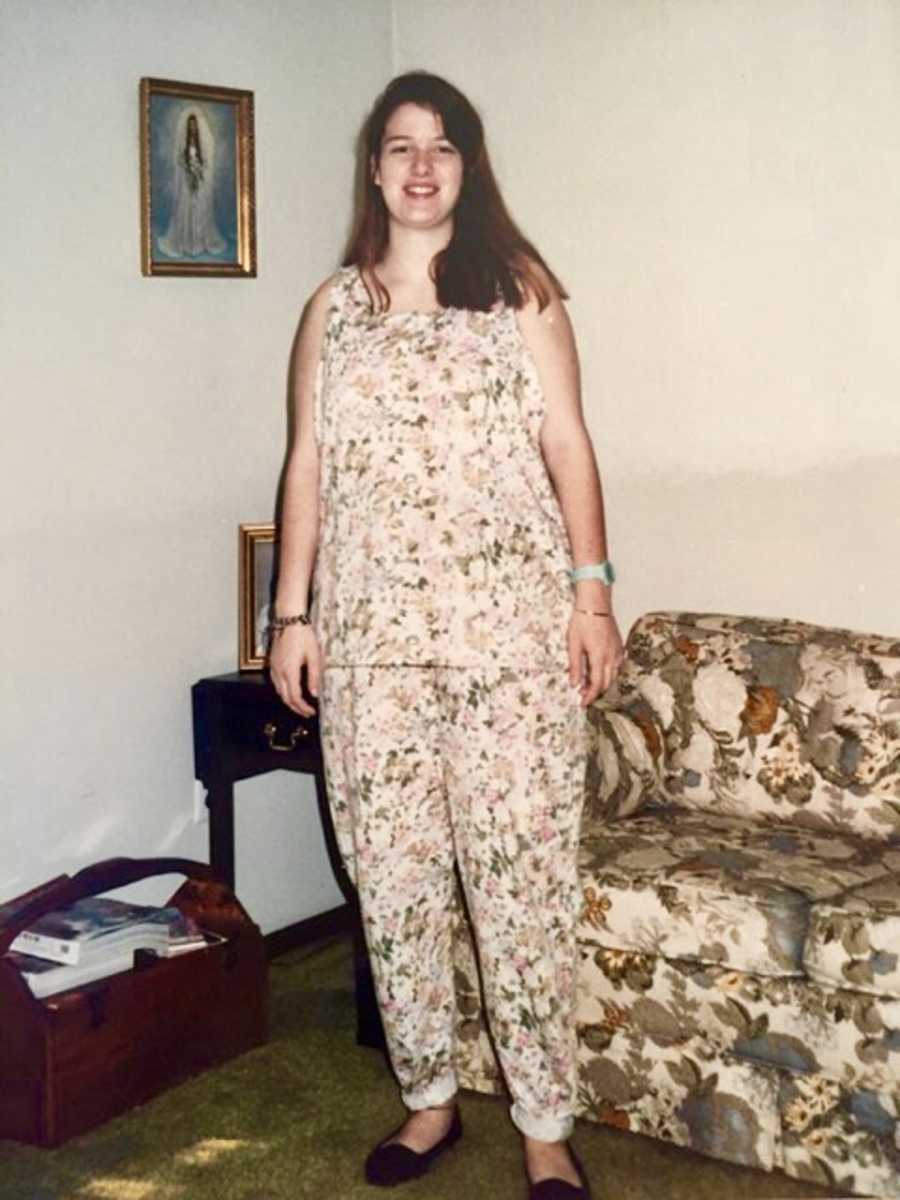 Pregnant teen stands smiling in floral outfit in home
